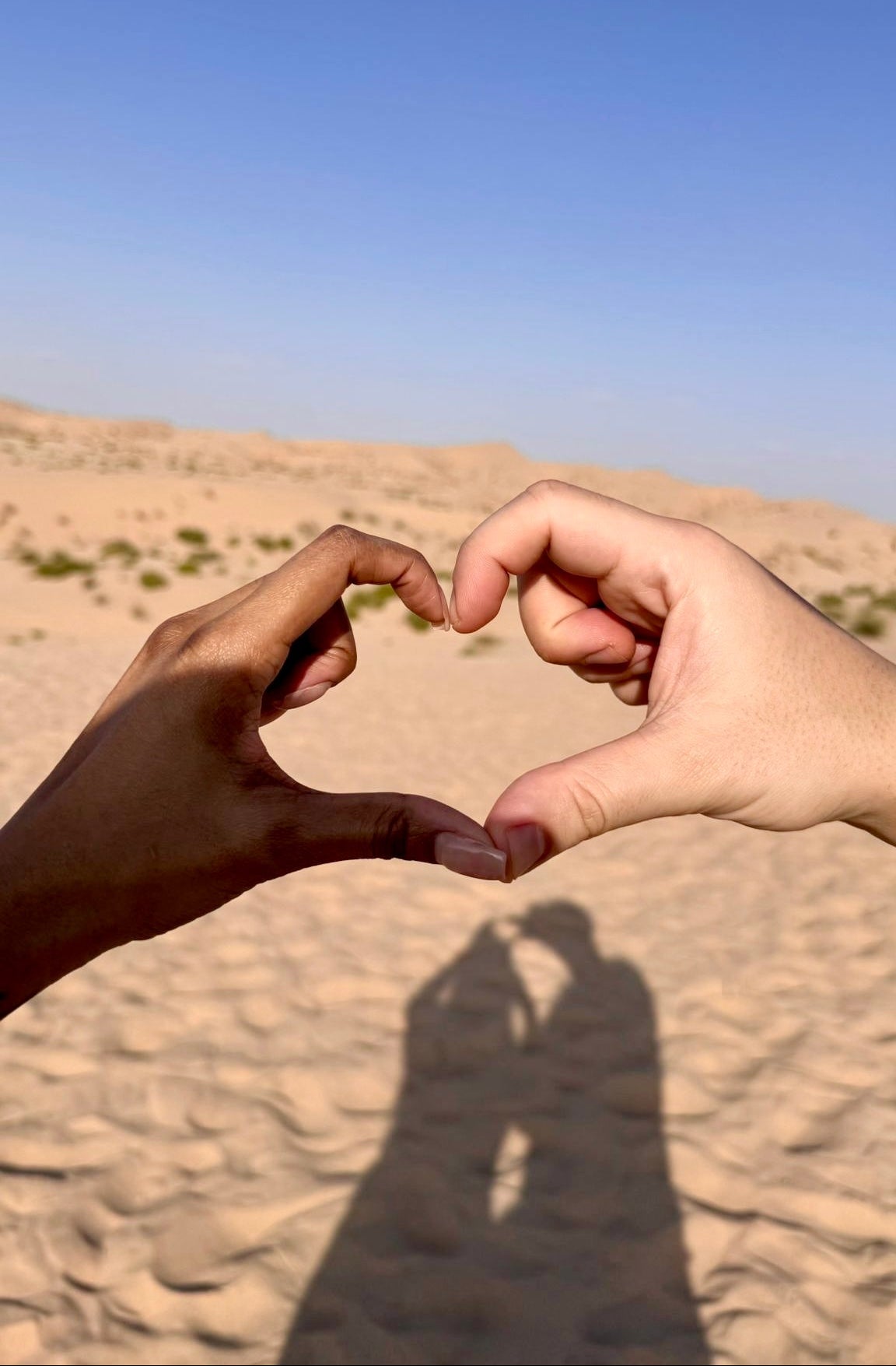 Two hands making a heart shape against a desert backdrop with a clear blue sky.