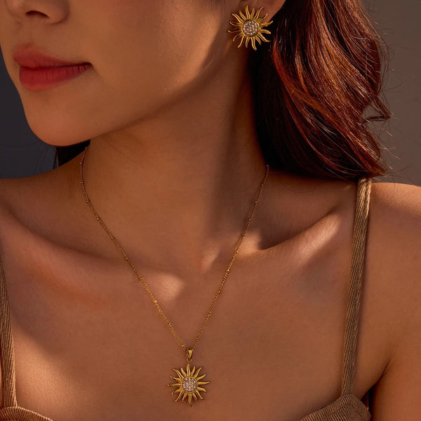 Close-up of a woman wearing gold sun-shaped earrings and necklace against a neutral background