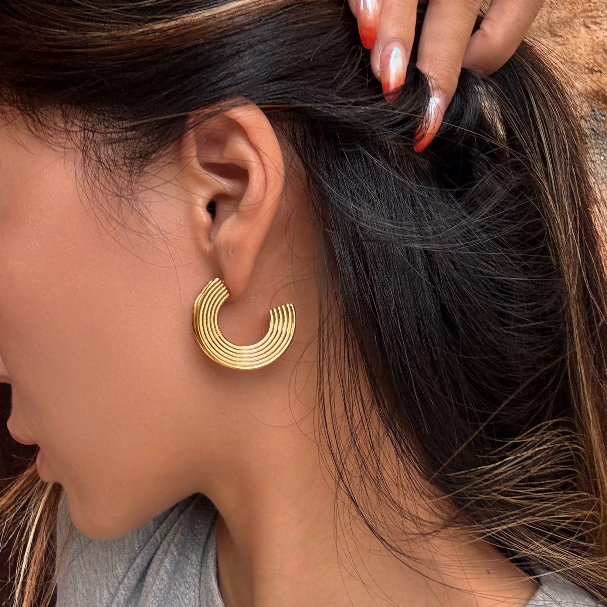 Close-up of a person wearing gold hoop earrings with a blurred background